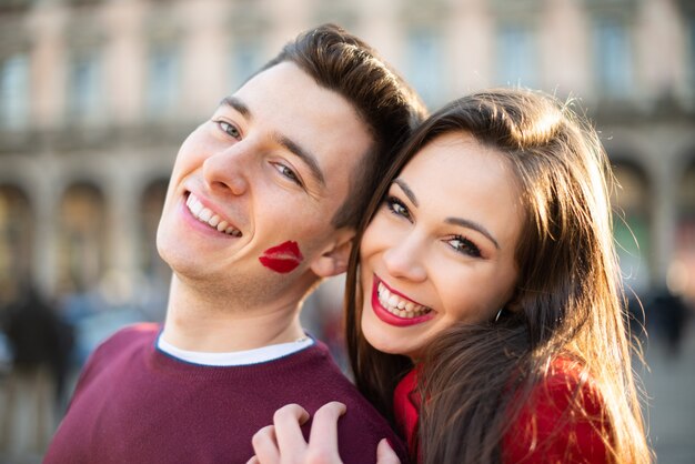 Ritratto sorridente delle coppie, l'uomo ha un segno di bacio del rossetto sulla sua guancia