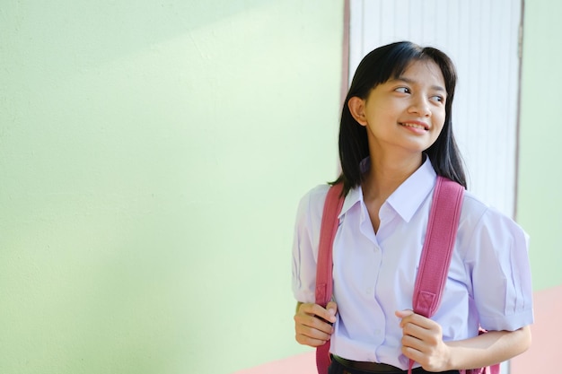 Ritratto studentessa giovane a scuola uniforme e zaino su sfondo verde, ragazza asiatica, adolescente.