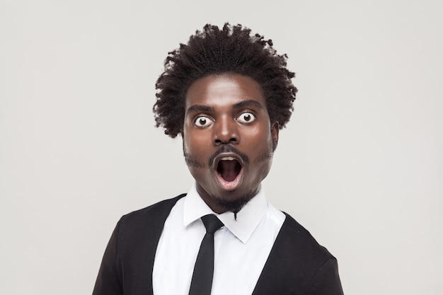 Ritratto stupito uomo afro con faccia scioccata. Studio girato, isolato su sfondo grigio