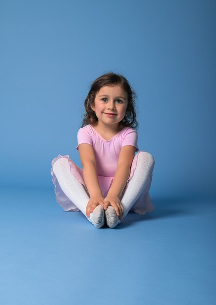 Ritratto su uno sfondo blu di una ballerina carina in un abito rosa che allunga il suo corpo.