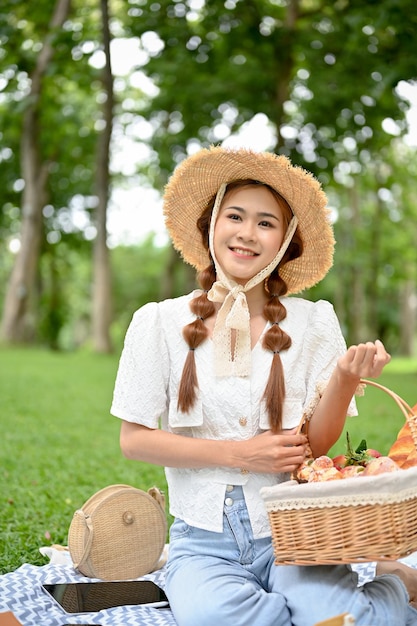 Ritratto Una bella giovane donna asiatica con un bel cappello di paglia si siede su una coperta da picnic