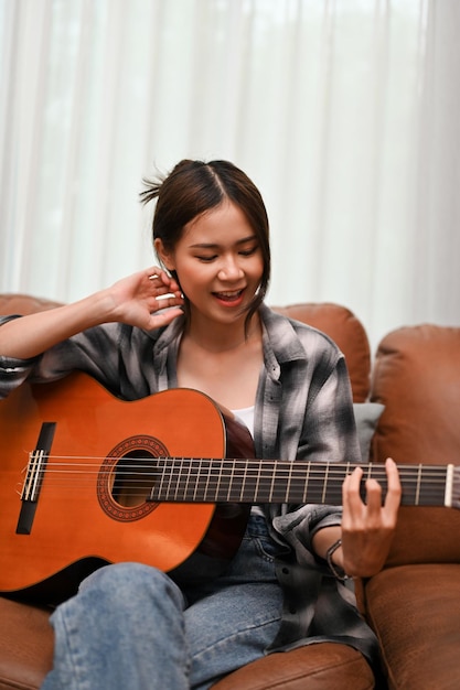 Ritratto Una donna asiatica attraente è sul divano a cantare e suonare la chitarra