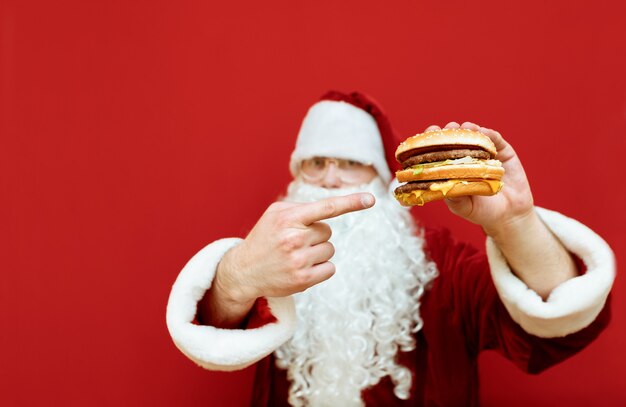 Ritratto uomo vestito da Babbo Natale che tiene hamburger