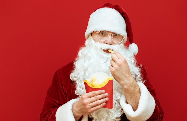 Ritratto uomo vestito da Babbo Natale che tiene patatine fritte