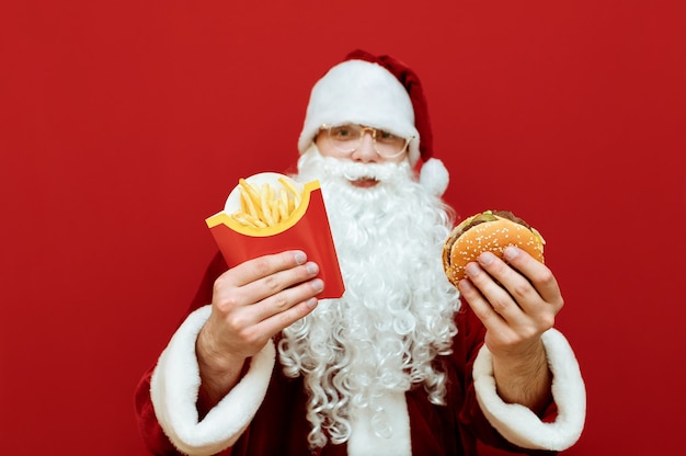 Ritratto uomo vestito da Babbo Natale tenendo hamburger e patatine fritte