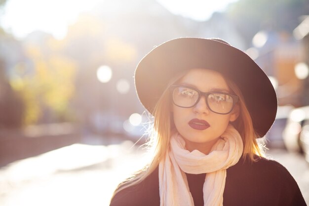 Ritratto urbano di donna bionda di lusso con labbra rosse con occhiali e cappello. Spazio per il testo