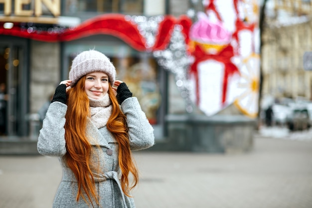 Ritratto urbano di una gioiosa donna zenzero con i capelli lunghi che indossa abiti caldi che camminano in città