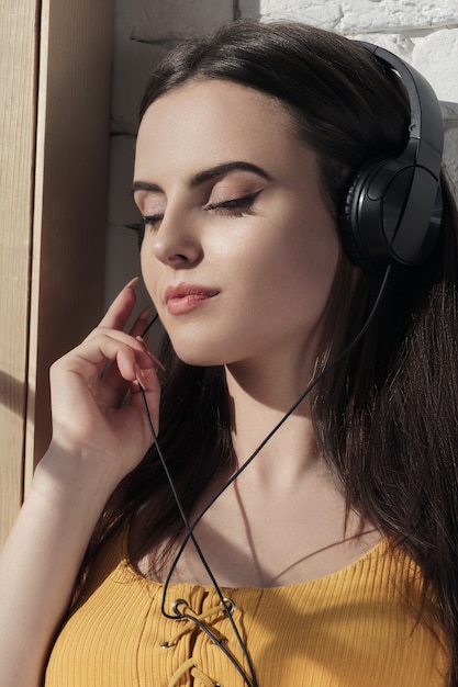 Ritratto verticale della ragazza che ascolta la musica in cuffie con gli occhi chiusi