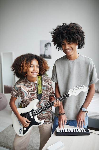 Ritratto verticale di due giovani afroamericani che suonano musica a casa e sorridono alla telecamera, fratello e sorella