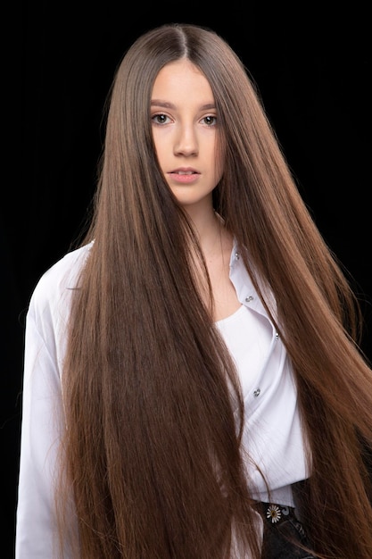 Ritratto verticale di una bella ragazza con capelli lussuosi molto lunghi su uno sfondo scuro.