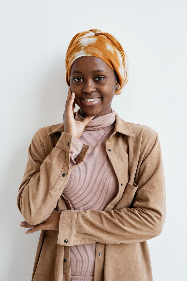 Foto ritratto verticale di una donna afroamericana sorridente che guarda la telecamera mentre sta in piedi contro il muro bianco
