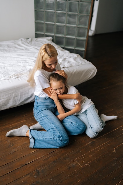 Ritratto verticale di una giovane madre amorevole e premurosa che conforta la piccola figlia triste offesa che mostra amore e cura che esprime sostegno abbracciando i capelli accarezzati