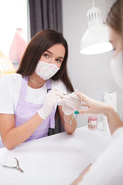 Ritratto verticale di una manicure professionista che indossa una maschera facciale che guarda la telecamera mentre lavora