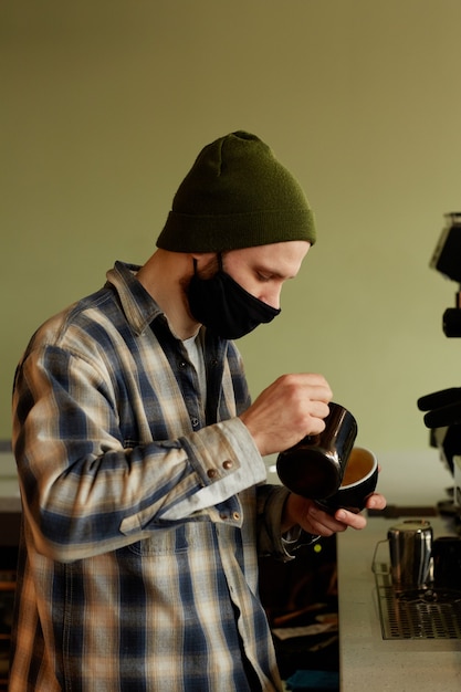 Ritratto verticale di vista laterale del barista maschio che prepara caffè fresco con crema mentre lavora al bar in caffetteria o caffetteria