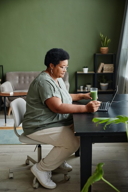 Ritratto verticale di vista laterale della donna anziana nera che utilizza il computer portatile a casa per lo shopping online