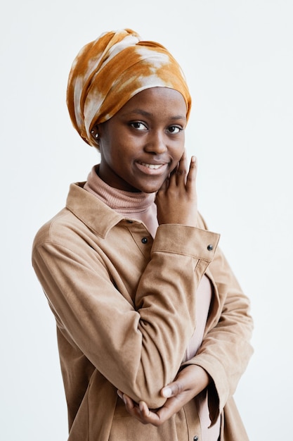 Ritratto verticale in vita di una donna afroamericana sorridente che guarda la telecamera mentre si trova contro il muro bianco