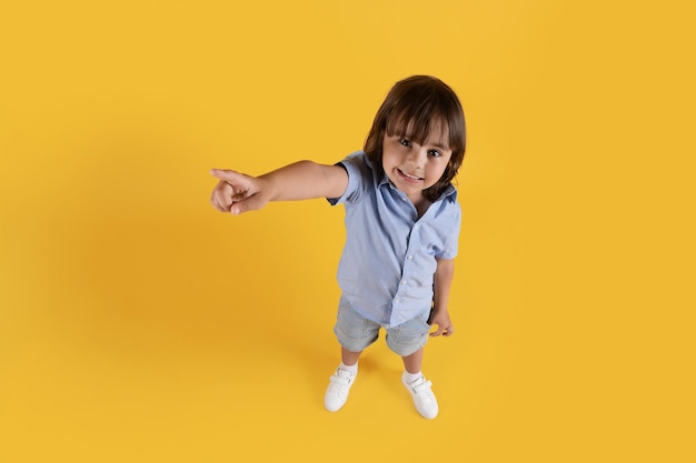 Ritratto vista dall'alto di un ragazzino carino che punta da parte allo spazio libero e sorridente sfondo giallo studio
