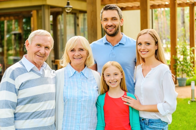 Riunione di famiglia. Una famiglia felice di cinque persone che si legano l'una all'altra e sorridono mentre stanno insieme nel cortile sul retro della loro casa