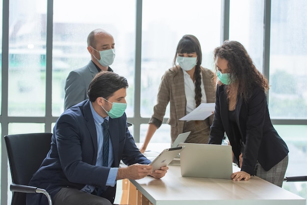 Riunione di gruppo di uomini d'affari in ufficio con maschera medica protetta nell'area di lavoro Gruppo di colleghi in abiti formali seduti al tavolo nella sala conferenze e che discutono del progetto di sviluppo aziendale