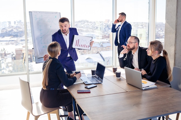 Riunione di successo di uomini d'affari, discussione di nuove idee imprenditoriali, utilizzo di diagrammi, seduta insieme. Sfondo ufficio moderno. Incontro di partner commerciali alla conferenza sullo sviluppo del business