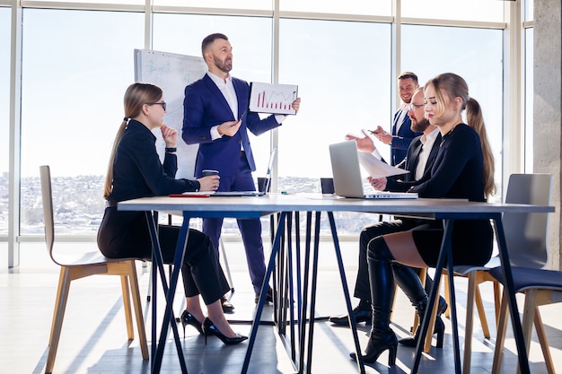 Riunione di successo di uomini d'affari, discussione di nuove idee imprenditoriali, utilizzo di diagrammi, seduta insieme. Sfondo ufficio moderno. Incontro di partner commerciali alla conferenza sullo sviluppo del business