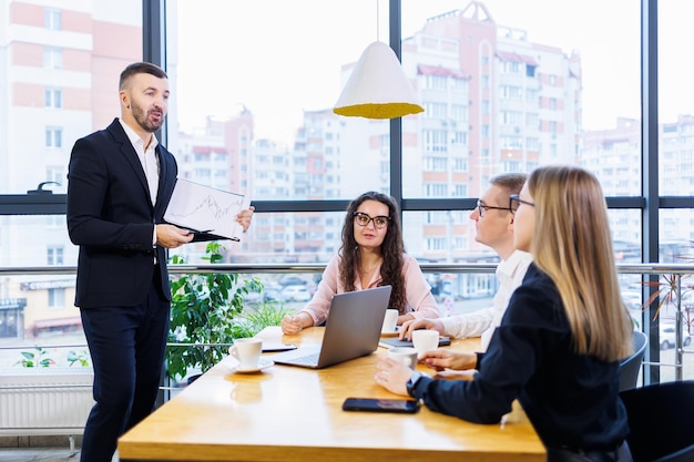 Riunione di successo di uomini d'affari, discussione di nuove idee imprenditoriali, utilizzo di diagrammi, seduta insieme. Sfondo ufficio moderno. Incontro di partner commerciali alla conferenza sullo sviluppo del business