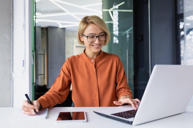 Riuscita donna d'affari soddisfatta sul posto di lavoro che lavora con il computer portatile all'interno dell'ufficio lavoratrice