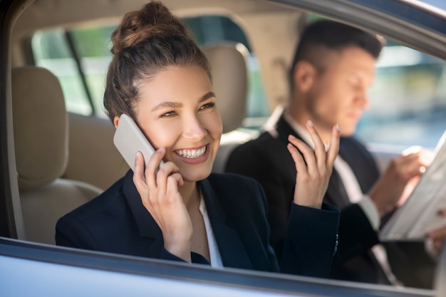 Riuscita donna sorridente che parla su uno smartphone in un'automobile