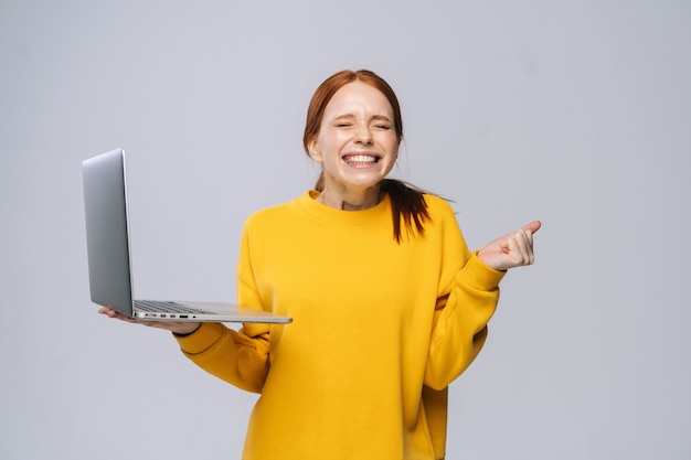 Riuscita giovane donna scioccata felice con gli occhi chiusi che tiene il computer portatile