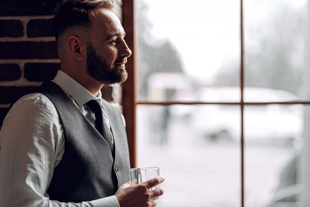 Riuscito giovane uomo d'affari in una giacca e cravatta. con un taglio ed una barba alla moda e alla moda. con in mano un bicchiere di whisky