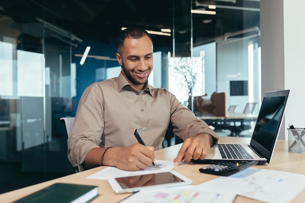 Riuscito uomo d'affari afroamericano all'interno dell'ufficio che fa lavoro di ufficio uomo che scrive lavoratore di informazioni