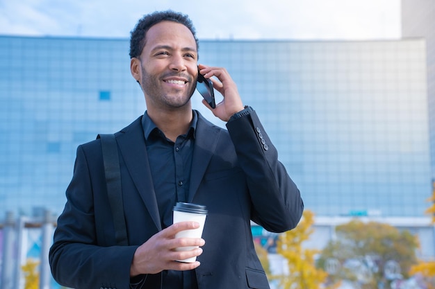 Riuscito uomo d'affari afroamericano in vestito che sorride felice che parla con il telefono astuto