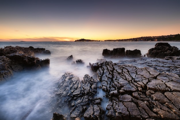 Riva del mare con rocce al tramonto Paesaggio marino in estate Rocce e acqua Esposizione lunga Mar Mediterraneo Immagine di viaggio