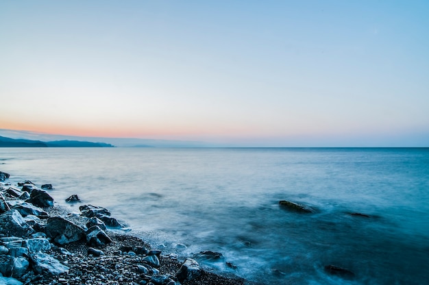 Riva del mare e spiaggia rocciosa, cielo azzurro con nuvole bianche