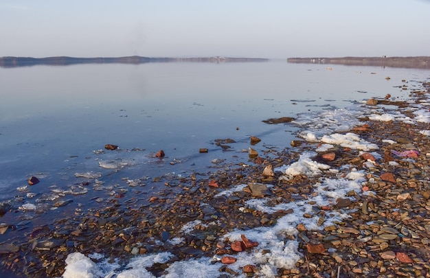 Riva del mare ricoperta di neve che si scioglie e una superficie d'acqua simile a uno specchio