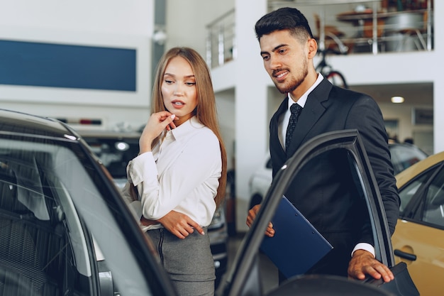 Rivenditore di auto uomo che mostra un acquirente donna una nuova auto nel salone dell'auto