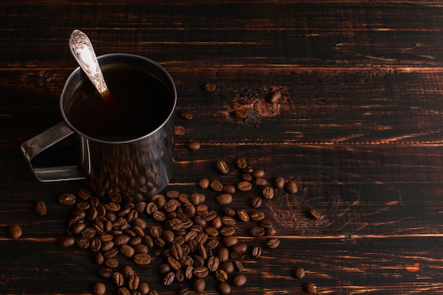 Rivesta di ferro la tazza con caffè nero e chicchi di caffè su una tavola di legno. copyspace.