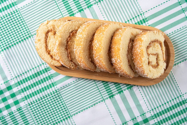 Rocambole, affettato â€‹â€‹rocambole farcito con dulce de leche su un vassoio di legno su un tavolo con tovaglia a scacchi. sfondo scuro, vista dall'alto.