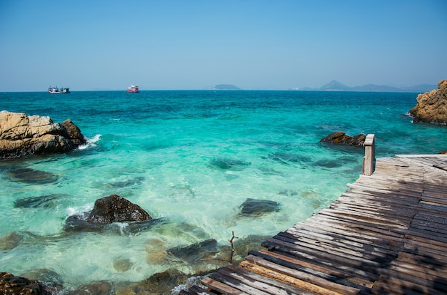 Rocce e ponte di legno sulla spiaggia con acqua di mare limpida