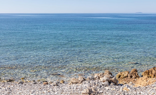 Rocciosa spiaggia vuota trasparente acqua di mare calmo cielo blu chiaro sullo sfondo Vista sul mare greca giornata di sole