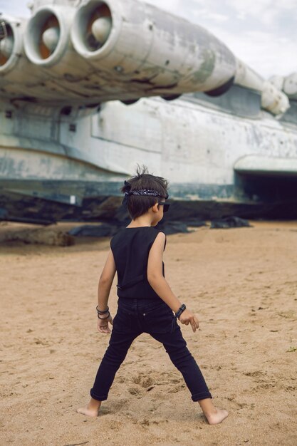Rocker boy un bambino in abiti neri si erge sullo sfondo di un aereo abbandonato sulla spiaggia