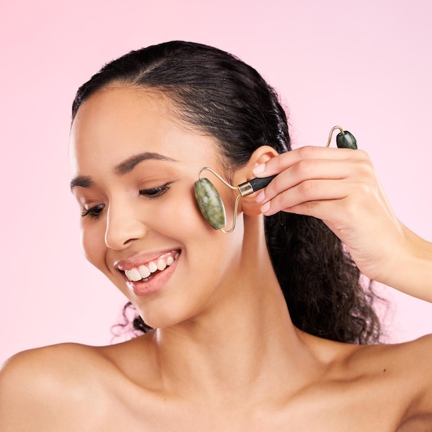 Roller facciale di bellezza naturale e donna con pelle luminosa cosmetici per la salute o il benessere Il viso di una giovane modella femminile estetica felice di risultati di massaggio dermatologico o di cura della pelle su uno sfondo rosa