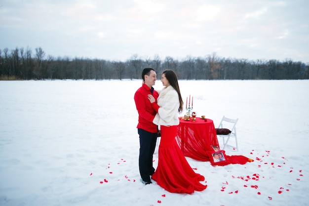 Romantica bella storia d'amore di amanti in abiti rossi in posa seduto a un tavolo su uno sfondo di neve