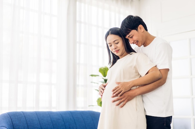 Romantica coppia asiatica dolce marito che abbraccia e sorride bellezza asiatica incinta wifeMan che si aspetta con la gravidanza della donna tenere il bambino nella pancia a casa