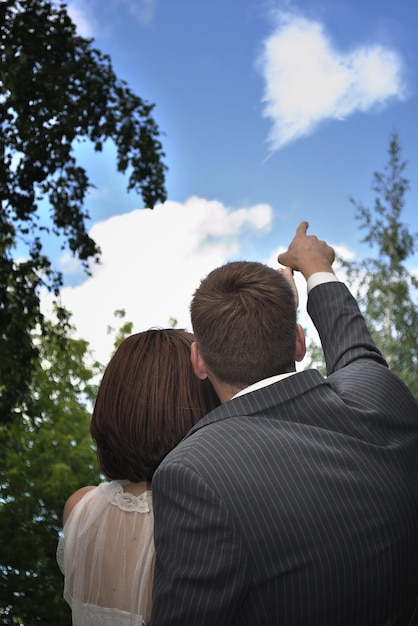 romantica coppia eterosessuale nel parco estivo guarda il cielo e la nuvola a forma di cuore