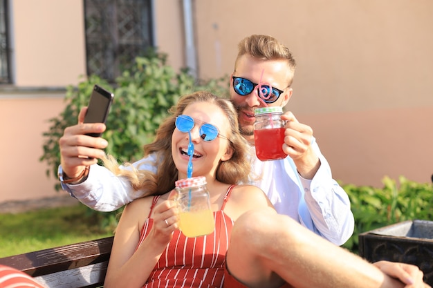 Romantica giovane coppia in abiti estivi sorridendo e prendendo selfie seduti su una panchina in una strada cittadina.