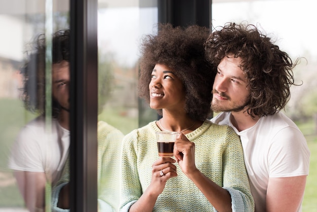 romantica giovane coppia multietnica felice che si gode il caffè del mattino vicino alla finestra nella loro casa di lusso