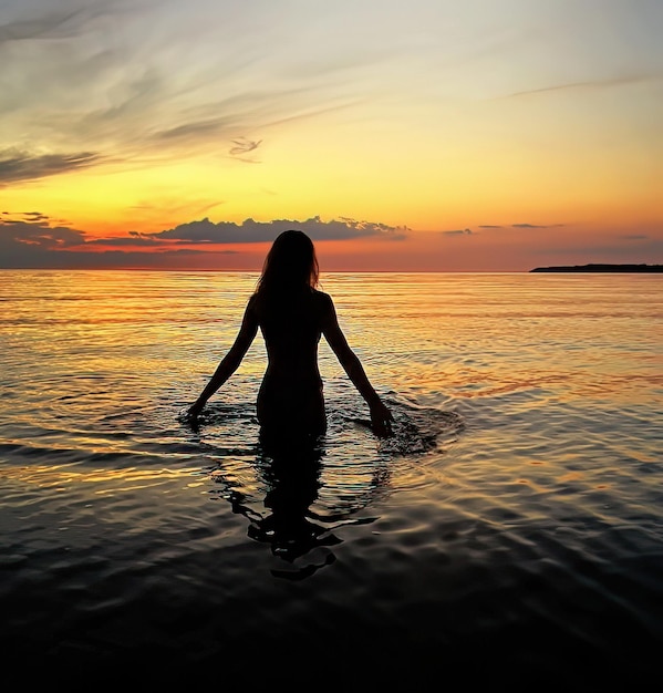 romantica giovane donna silhouette al tramonto arancione nell'onda di acqua di mare e cielo nuvoloso rosa