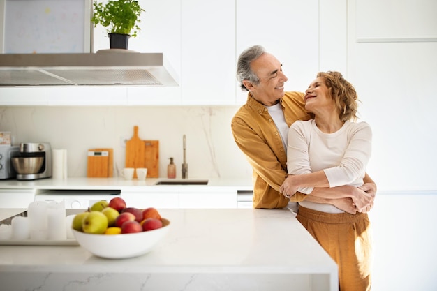 Romantici coniugi senior sposati che si abbracciano in cucina amorevole vecchia coppia che si gode il tempo insieme nello spazio libero di casa