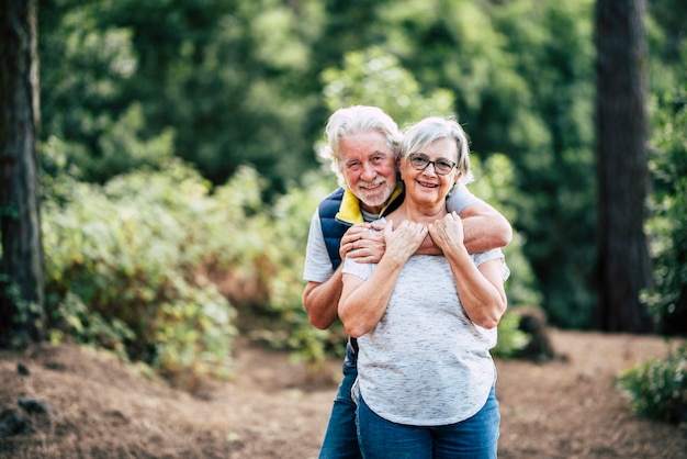 Romantico amorevole coppia senior felice godendo abbraccio mentre in piedi nella foresta, sorridente marito che abbraccia la moglie da dietro Ritratto di romantico invecchiamento vecchia coppia trascorrere il tempo libero nella foresta